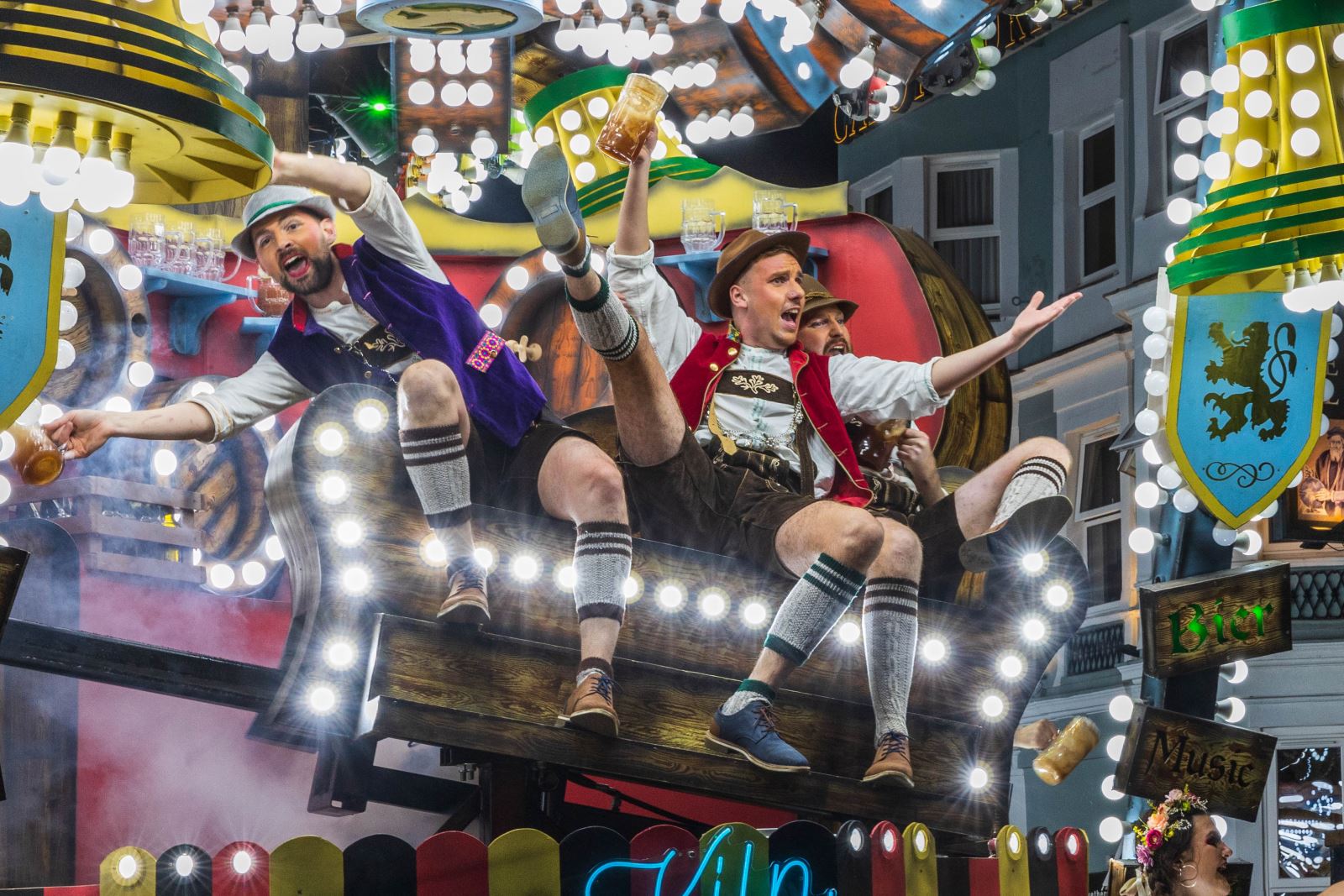 Three men in Lederhosen clutching beer jugs performing on top of an Oktoberfest-themed float at the Weston-super-Mare Carnival